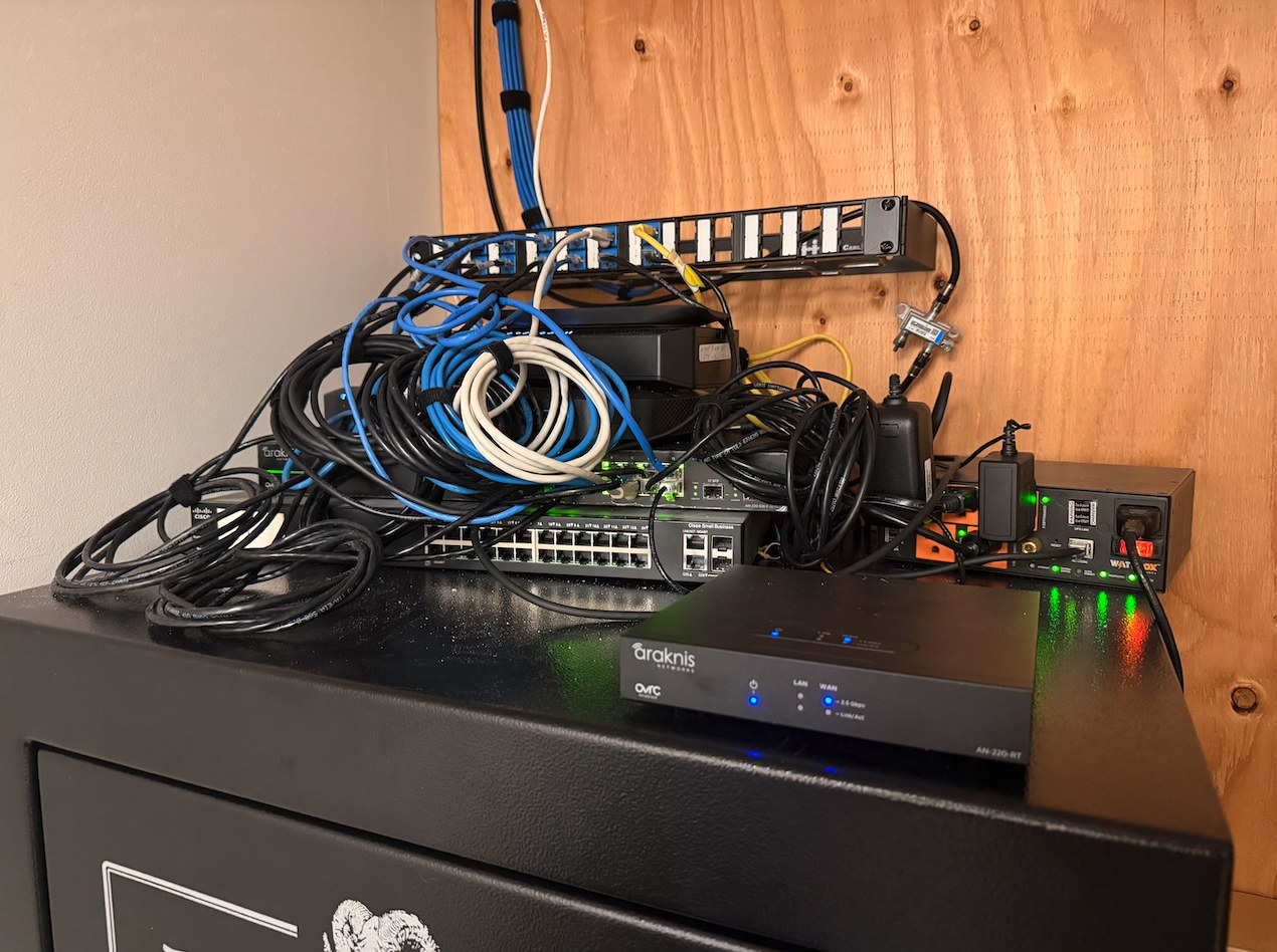 Photo of the current equipment closet: gear stacked on a black safe with a tangle of cables